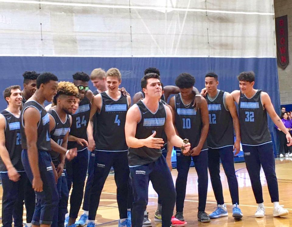 Student councils (including ESC) helped kick-off Columbia's basketball season.Columbia's boy's basketball team dressed in their blue jerseys and sweatpants huddle together, some with their arms around each other, in the school gymnasium while one of the boys is front and center in mid-phrase while they're all singing along.